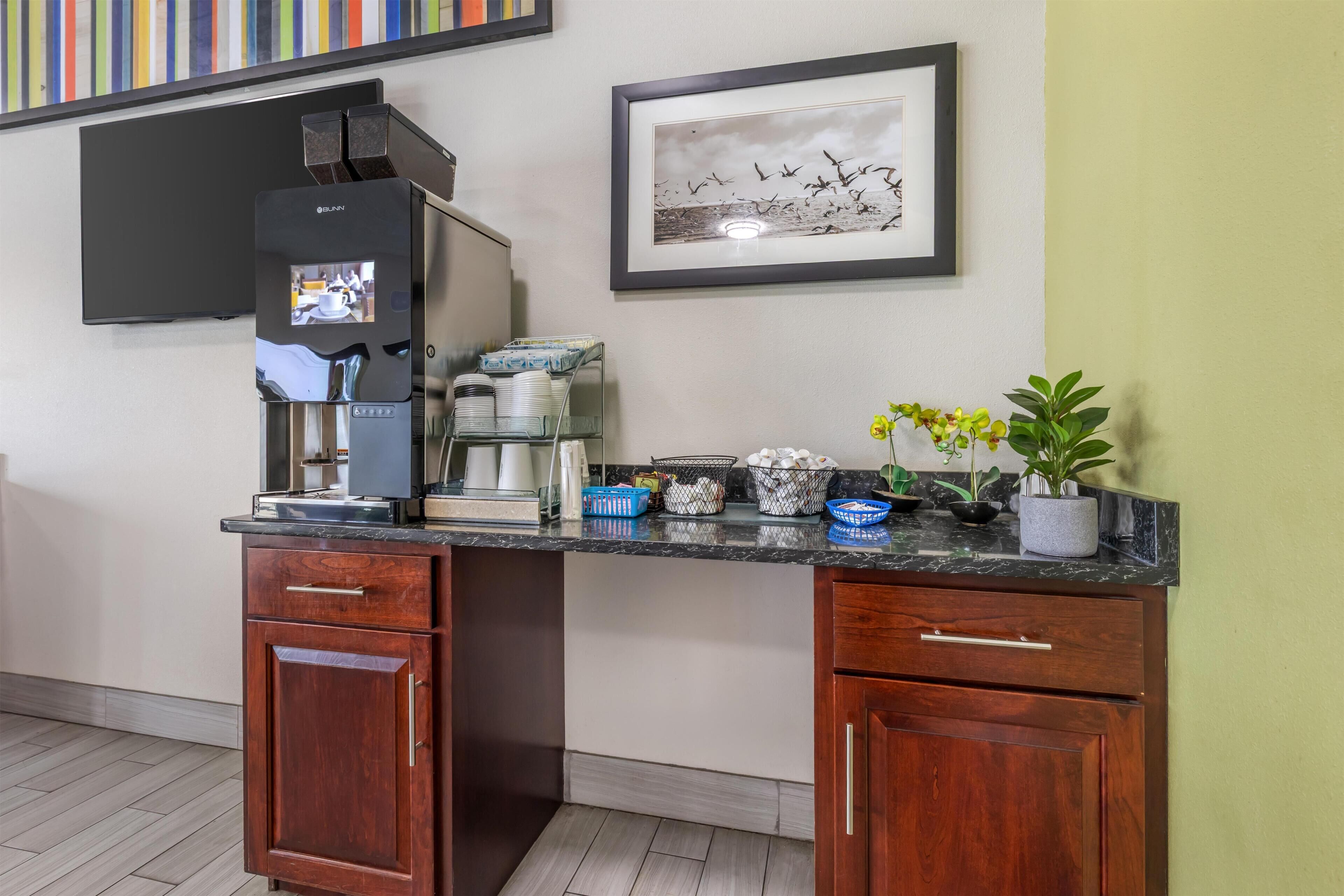 A kitchenette with a coffee machine, a framed picture, and a potted plant.