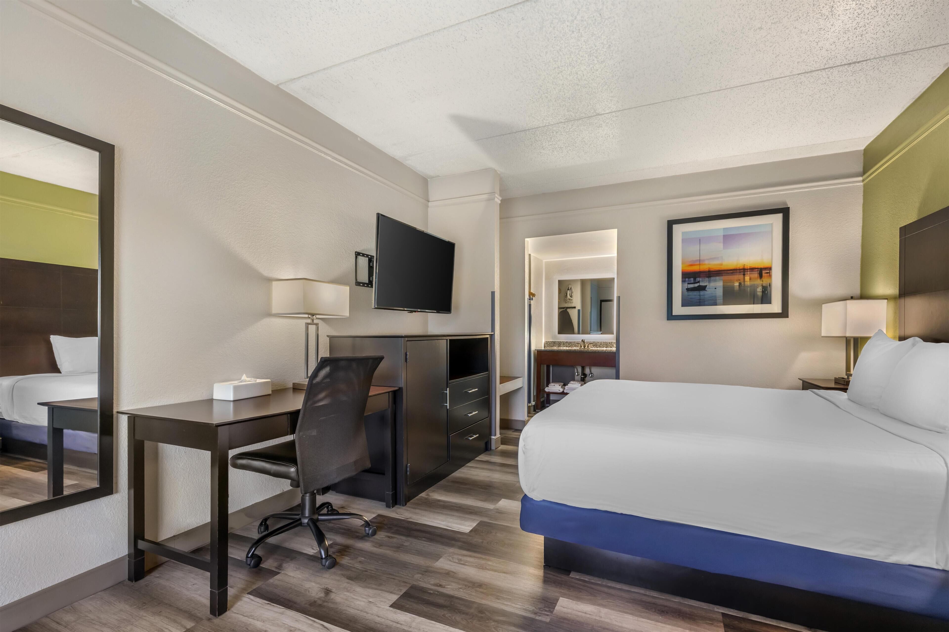 Ein Hotelzimmer mit Bett, Schreibtisch, Stuhl, Fernseher und einem Gemälde an der Wand.