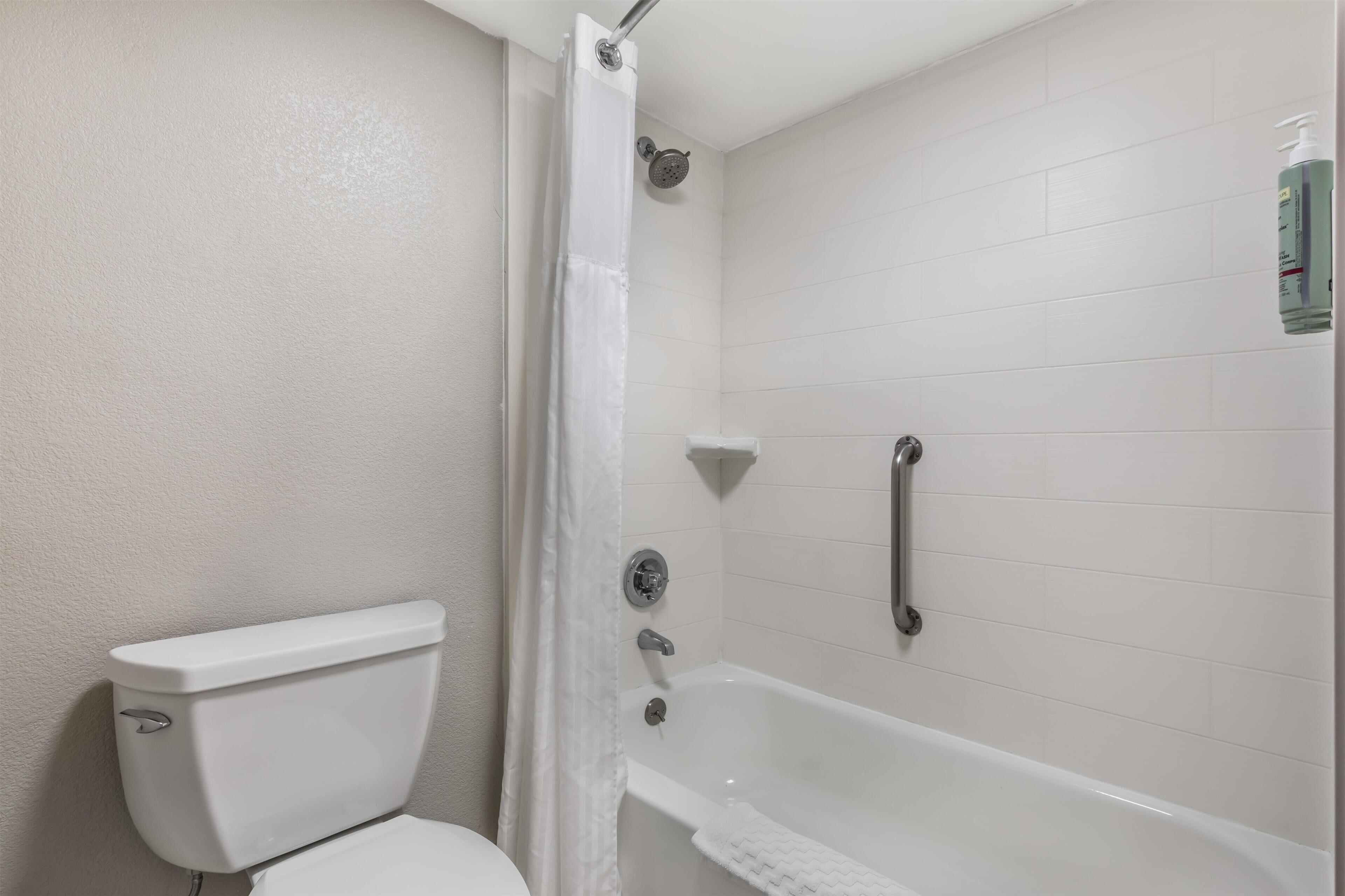 Un baño con inodoro blanco, ducha con cortina y bañera.