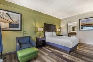 A hotel room with a bed, a chair, a nightstand, a lamp, and a painting on the wall.