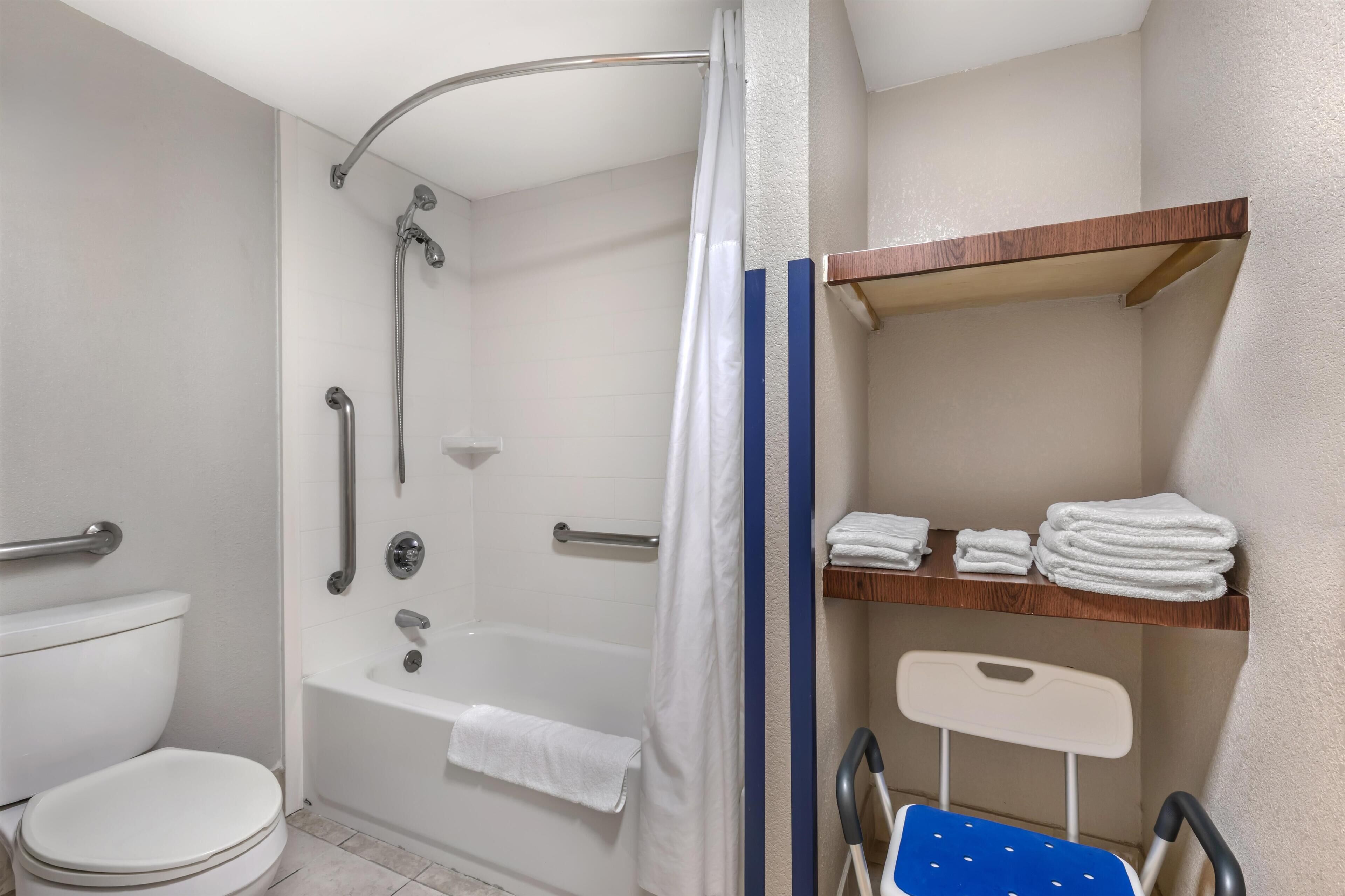 A bathroom with a shower, toilet, and a wheelchair-accessible chair.