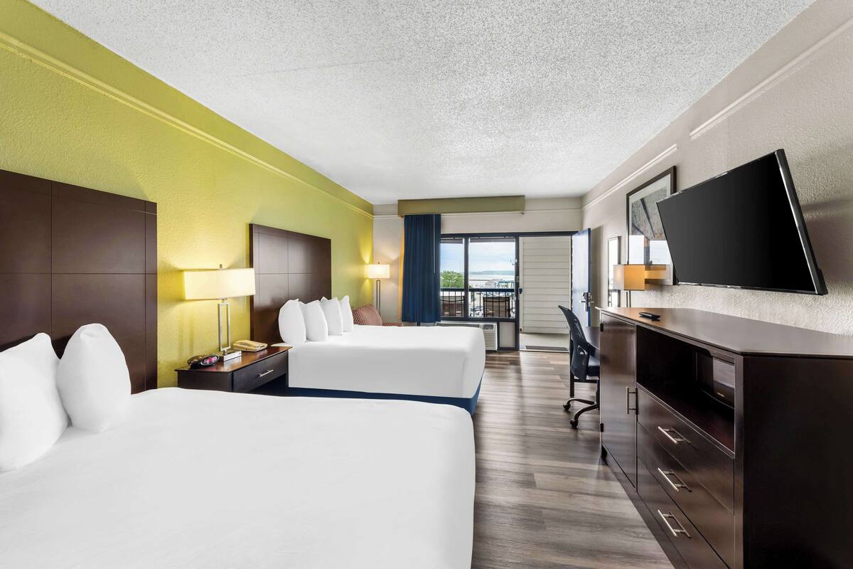 A hotel room with two beds, a desk, a TV, and a view of the outdoors.