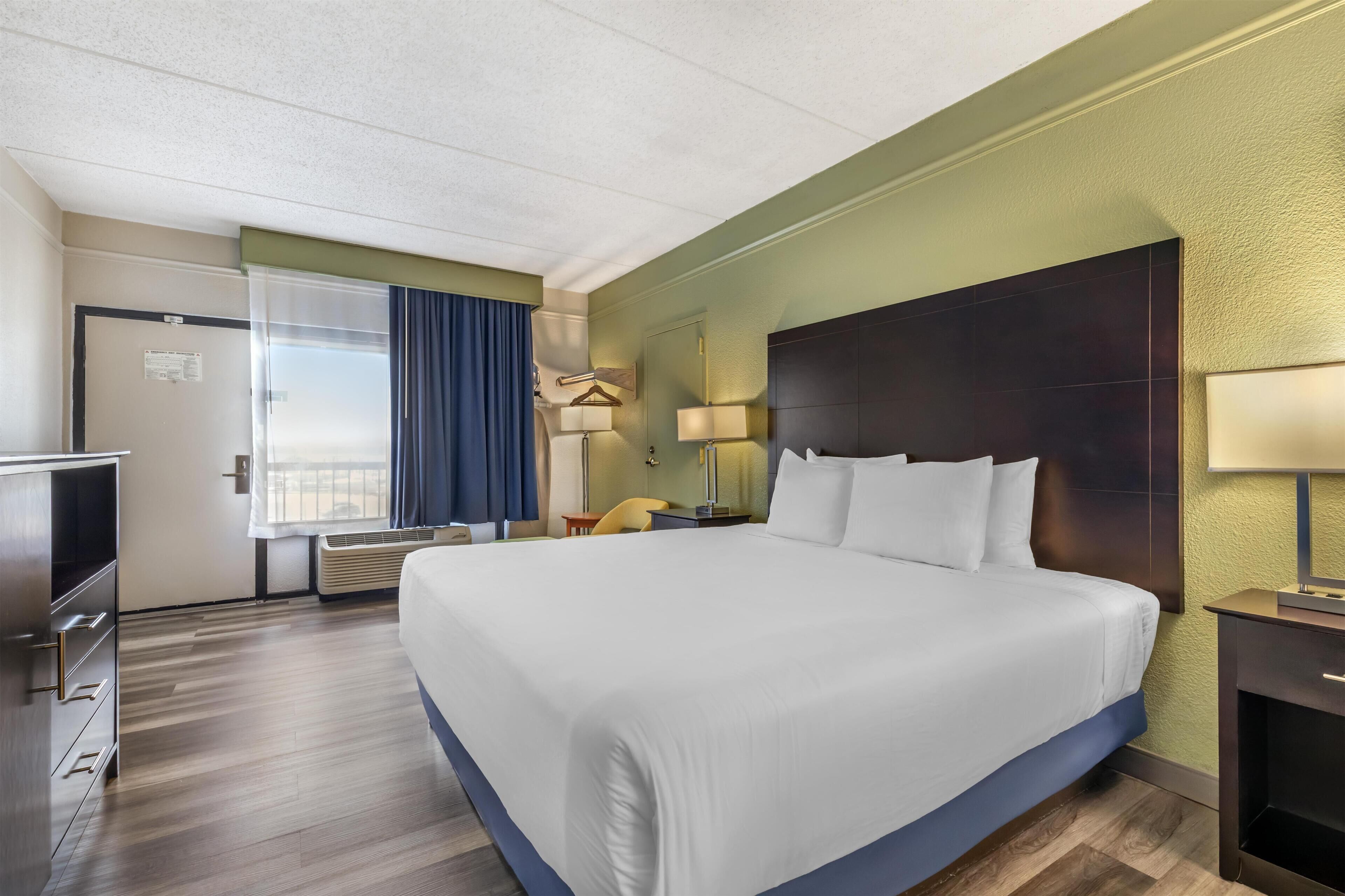 A hotel room with a large bed, a desk, a chair, a TV, and a window with curtains.