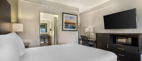 A hotel room with a large bed, a flat-screen TV, a desk with a chair, and a bathroom visible through an open door.
