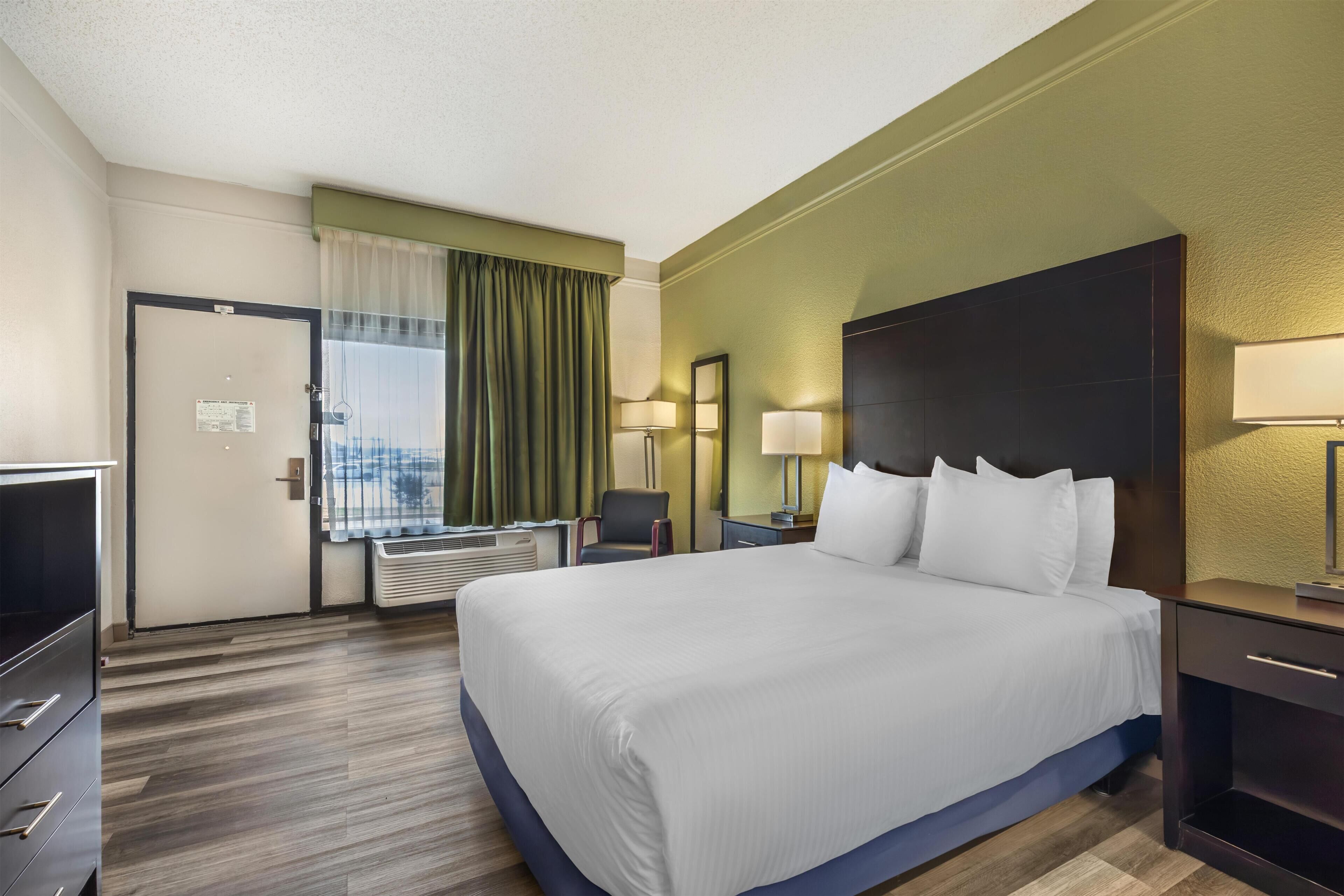 A hotel room with a large bed, a desk, a chair, two bedside lamps, and a window with curtains.