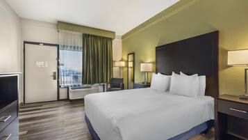 A hotel room with a large bed, a desk, a chair, two bedside lamps, and a window with curtains.