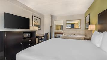 Quarto de hotel com cama grande, escrivaninha com cadeira, TV de tela plana, micro-ondas, banheiro com pia e espelho, e um espelho grande na parede.