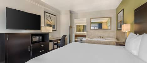 A hotel room with a large bed, a desk with a chair, a flat-screen TV, a microwave, a bathroom with a sink and mirror, and a large mirror on the wall.