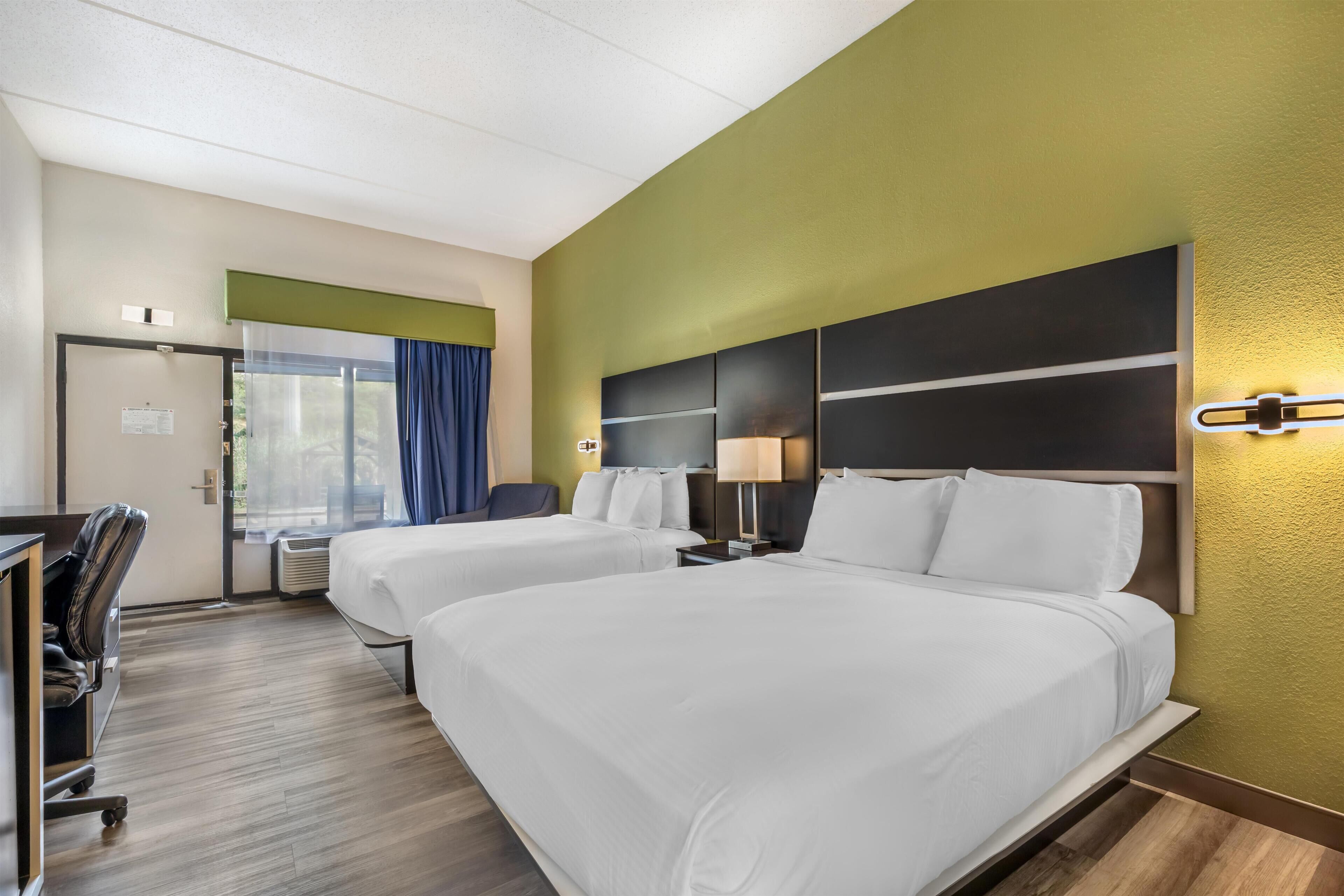 A hotel room with two beds, a desk, and a chair.