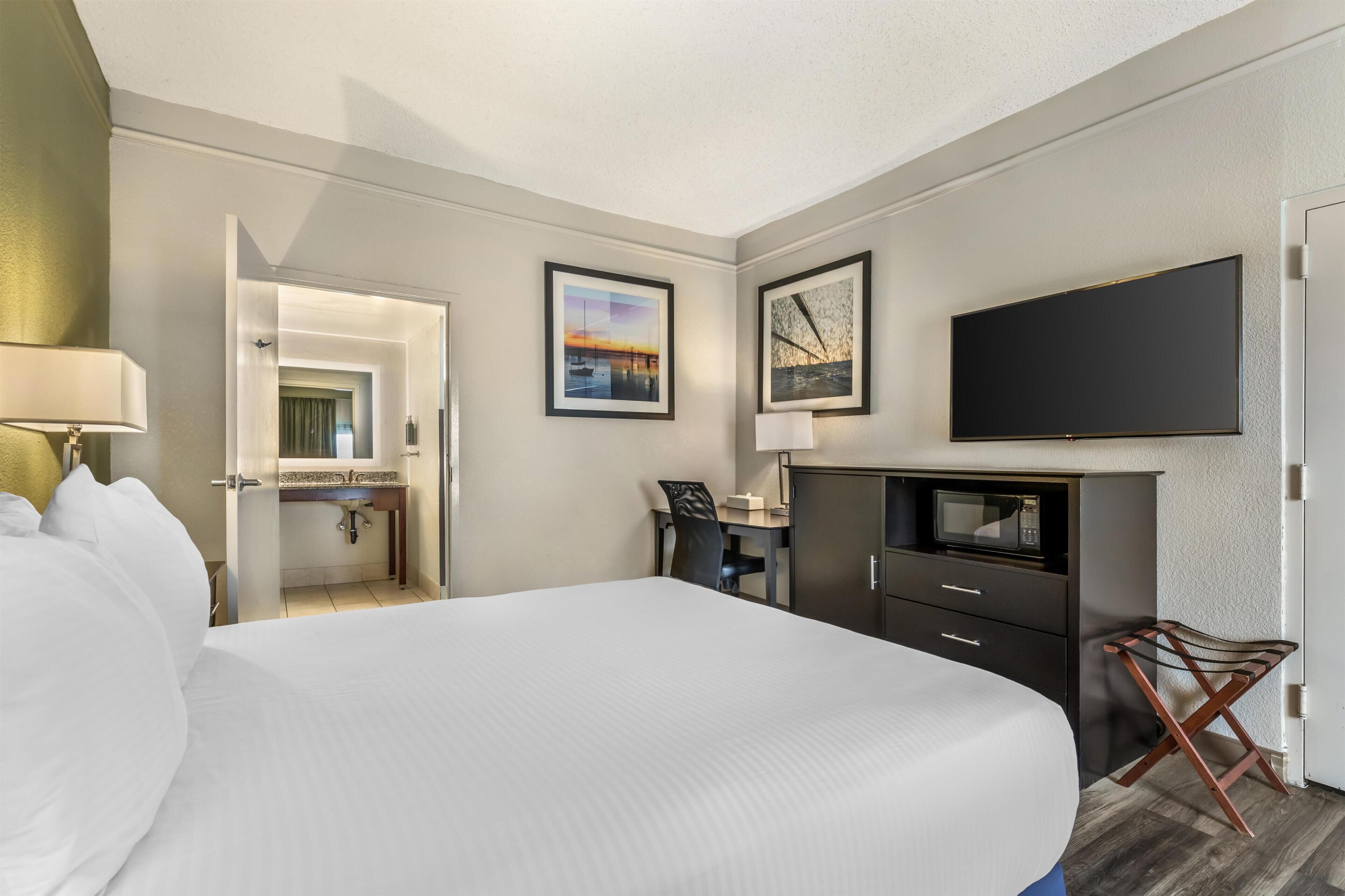 Quarto de hotel com cama, escrivaninha, TV de tela plana e obras de arte nas paredes.