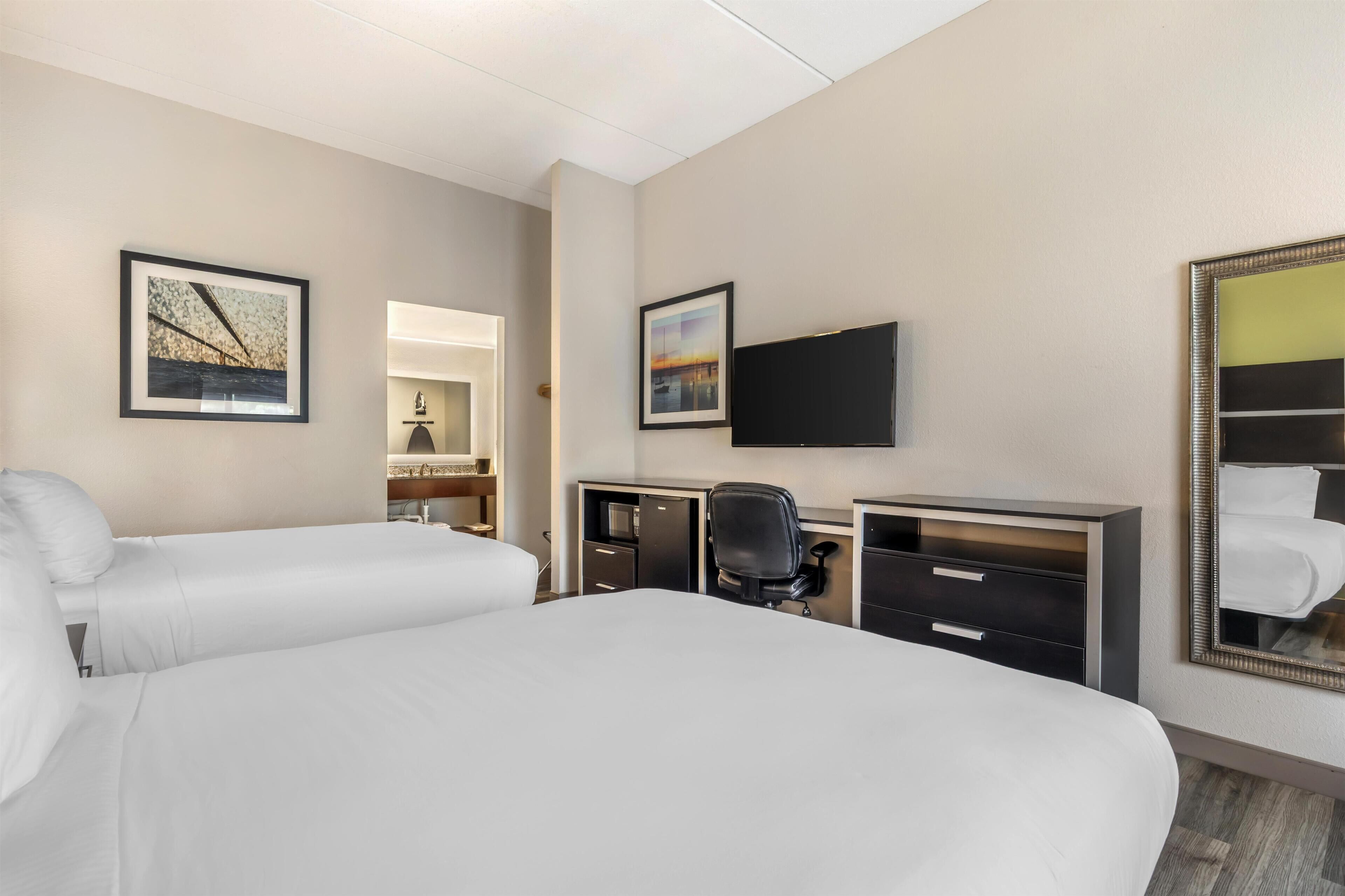 A hotel room with a bed, a desk, a chair, a television, and artwork on the walls.