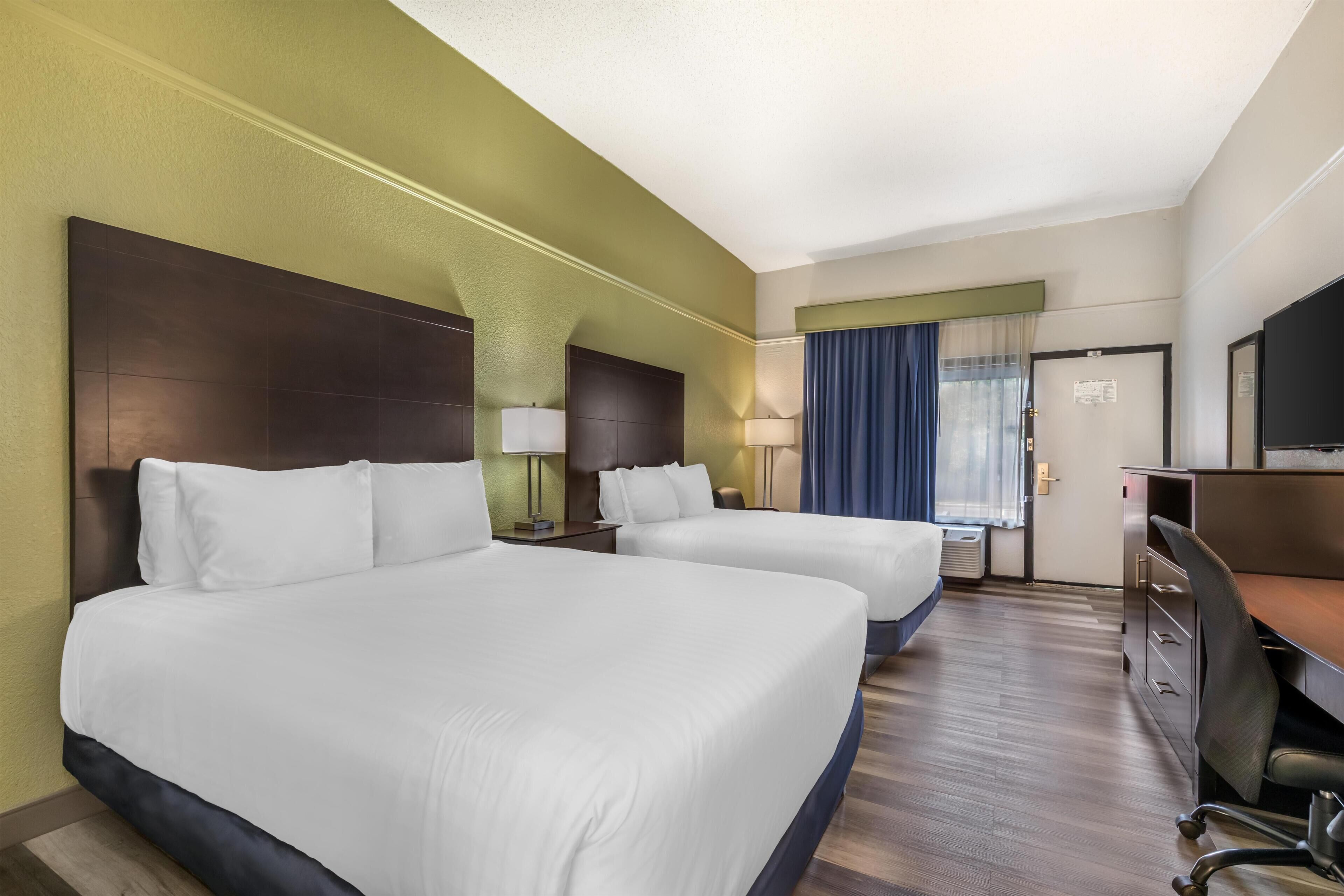 A hotel room with two beds, a desk, a chair, and a television.