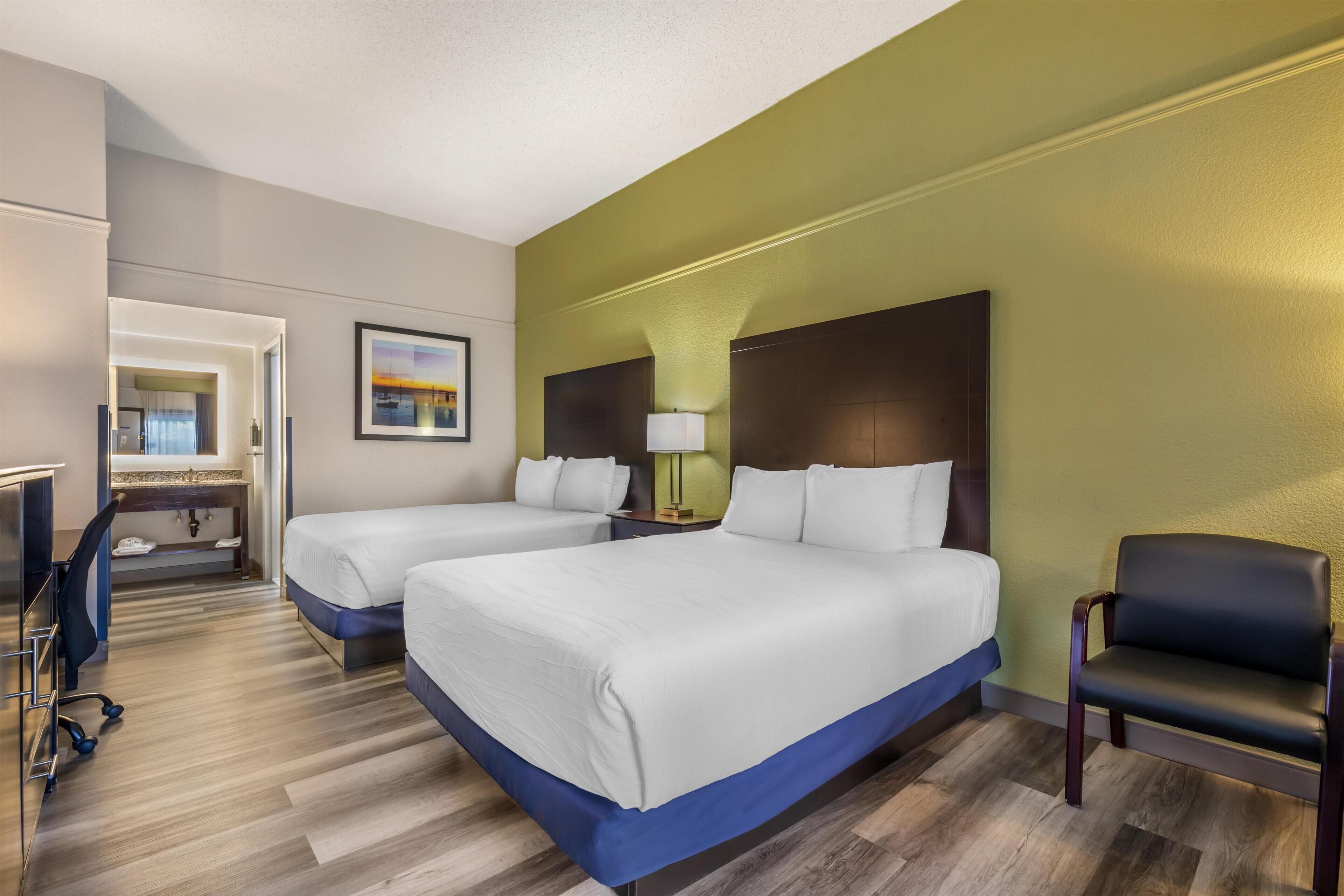 A hotel room with two beds, a desk, a chair, and a bathroom.