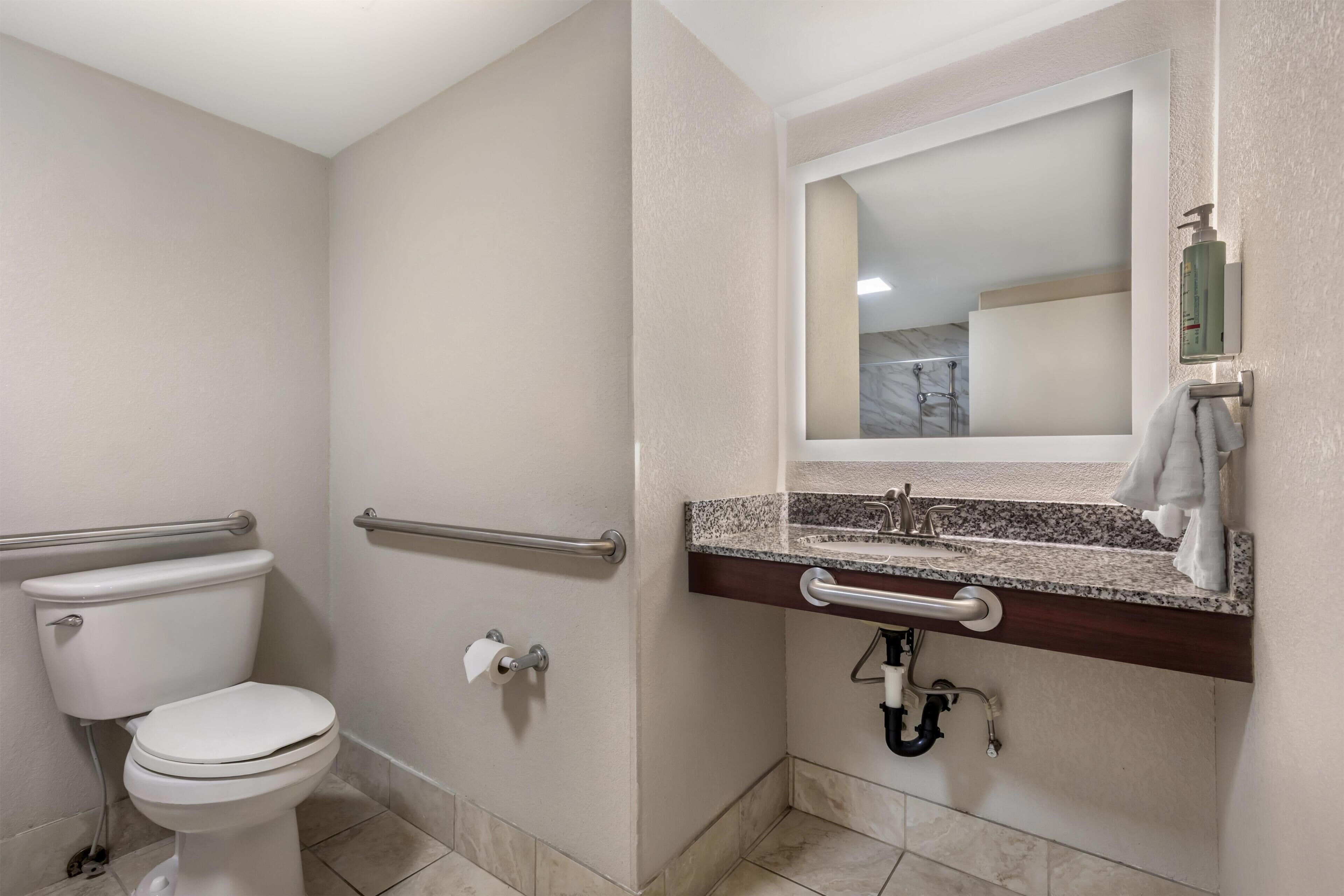 A bathroom with a toilet, a handrail, a sink with a mirror, and a towel rack.