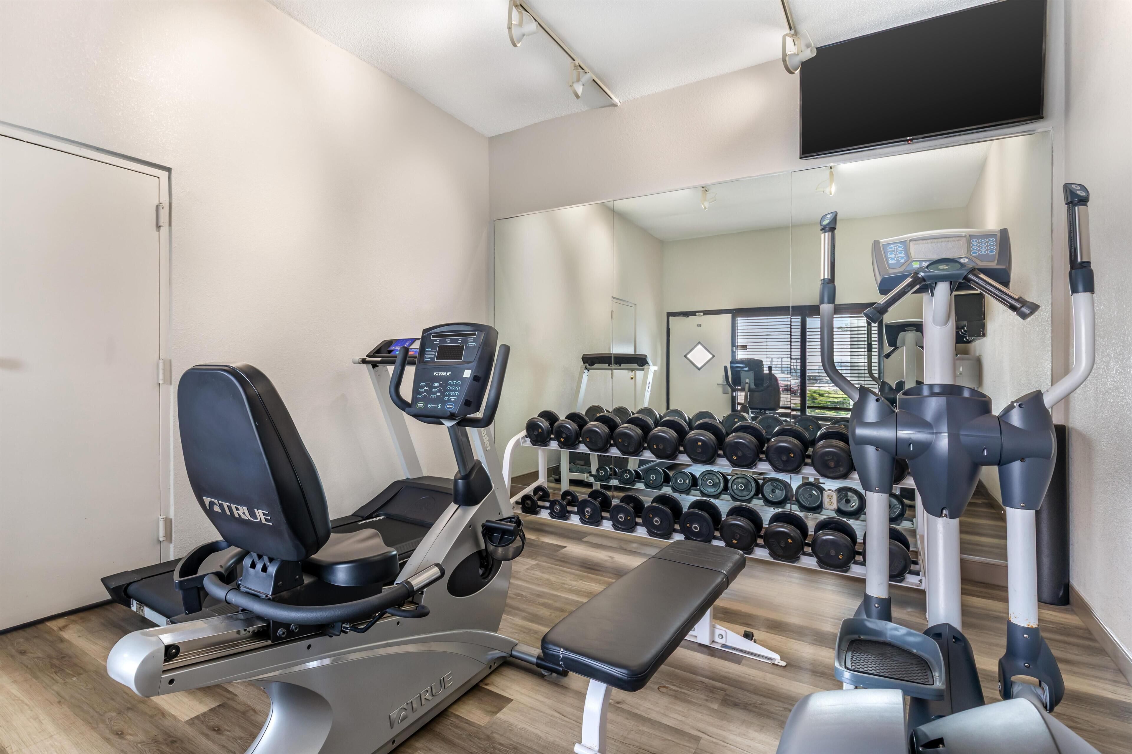 A gym with exercise equipment, a bench, and a wall-mounted mirror.