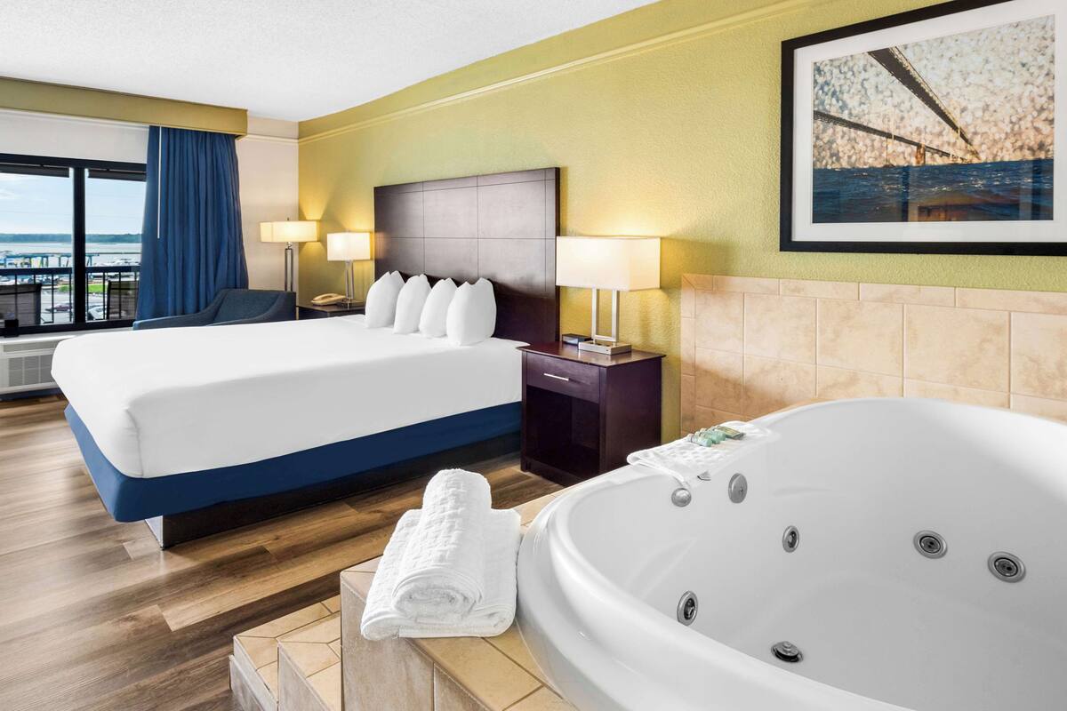 A hotel room with a large bed, a separate sitting area, a bathtub, and a view of the outdoors.