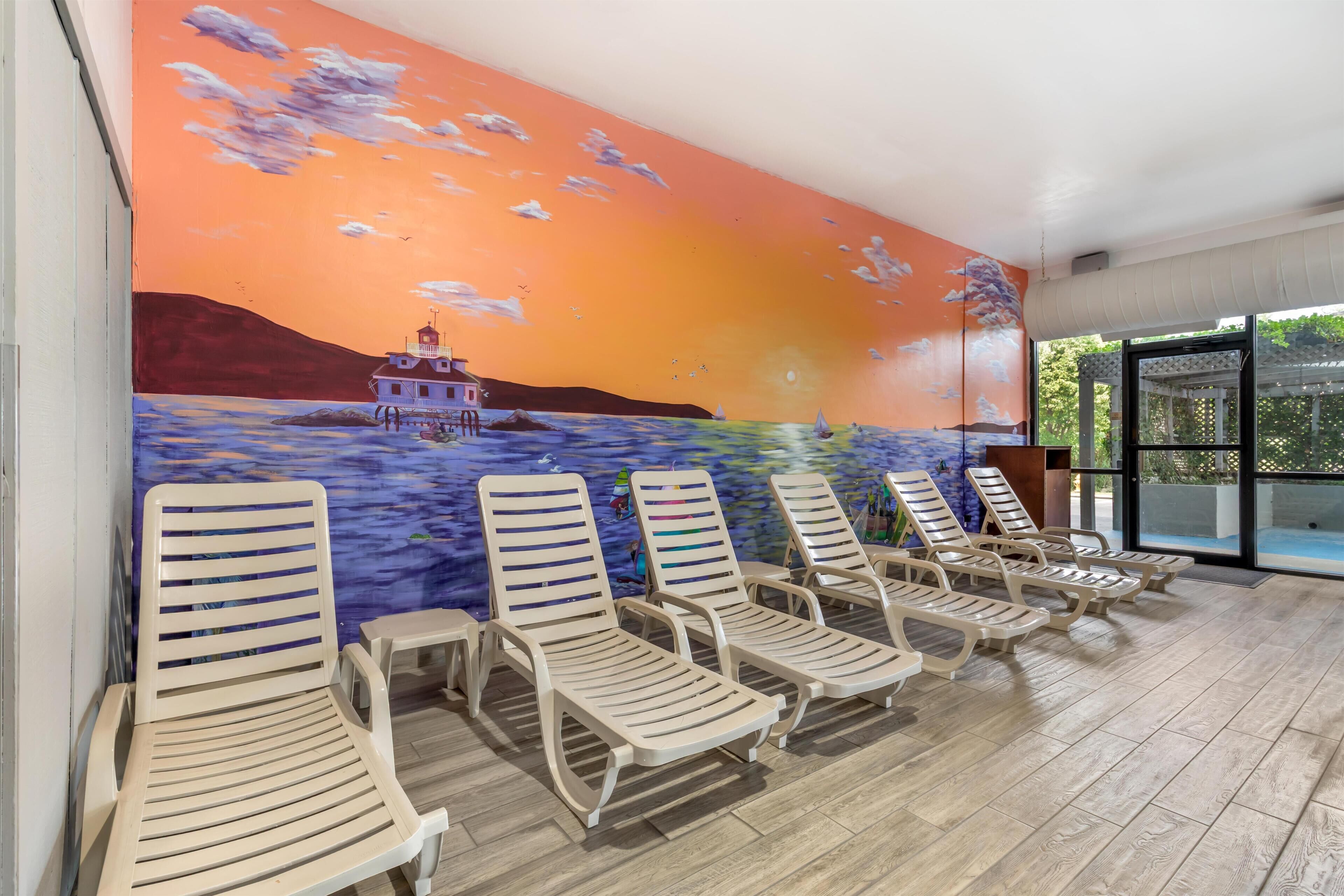 A poolside area with lounge chairs and a mural of a sunset over water.