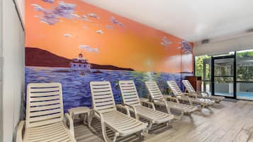 A poolside area with lounge chairs and a mural of a sunset over water.