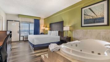 A hotel room with a bed, a desk, a chair, a large window with curtains, a wall-mounted painting, and a bathtub.