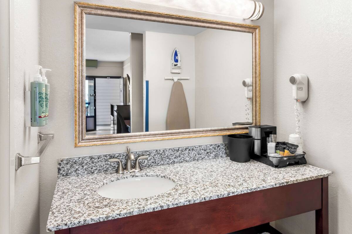 A bathroom with a granite countertop sink, a large mirror, and a hairdryer mounted on the wall.