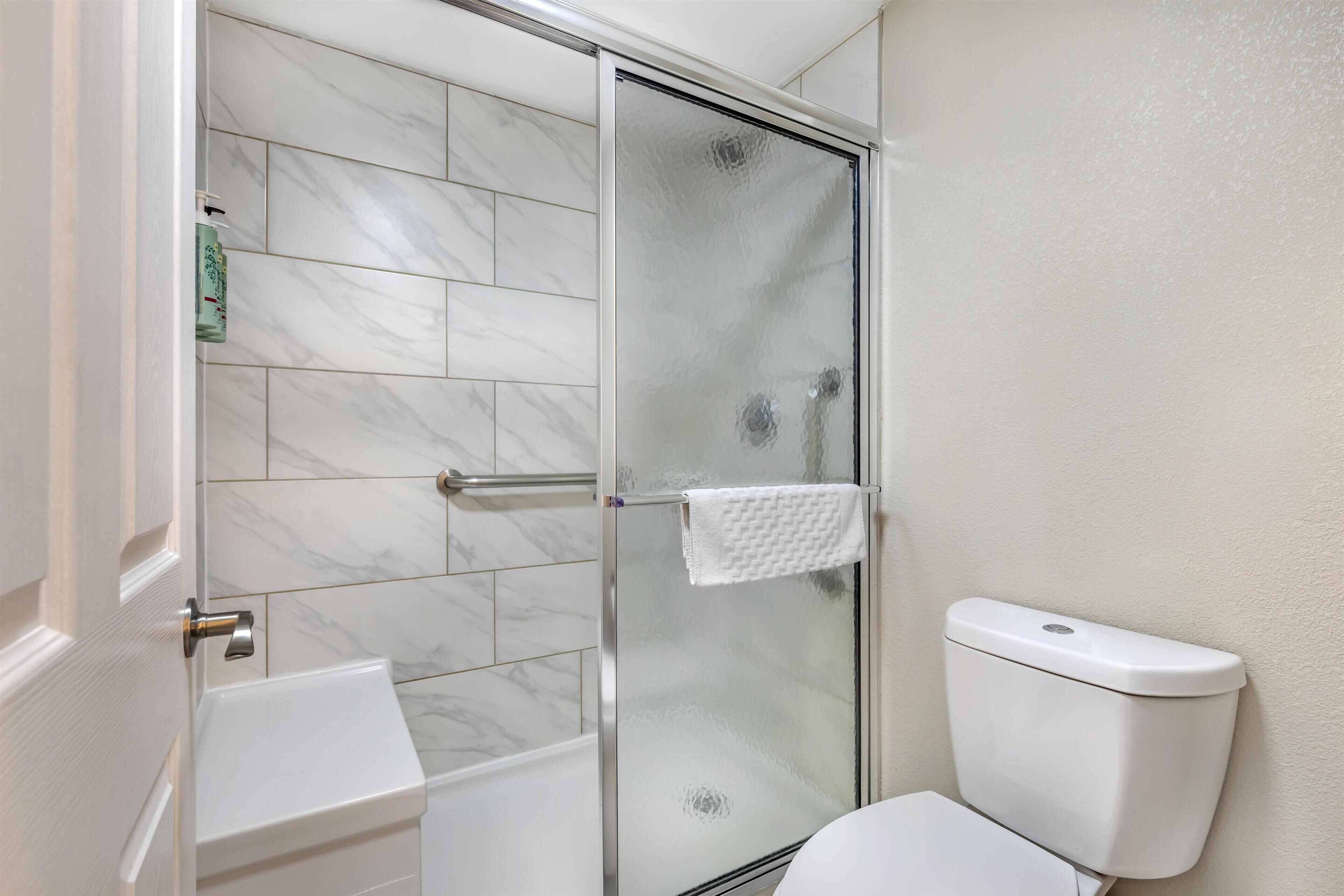 Un baño con ducha envuelta en vidrio, inodoro blanco y lavabo blanco.