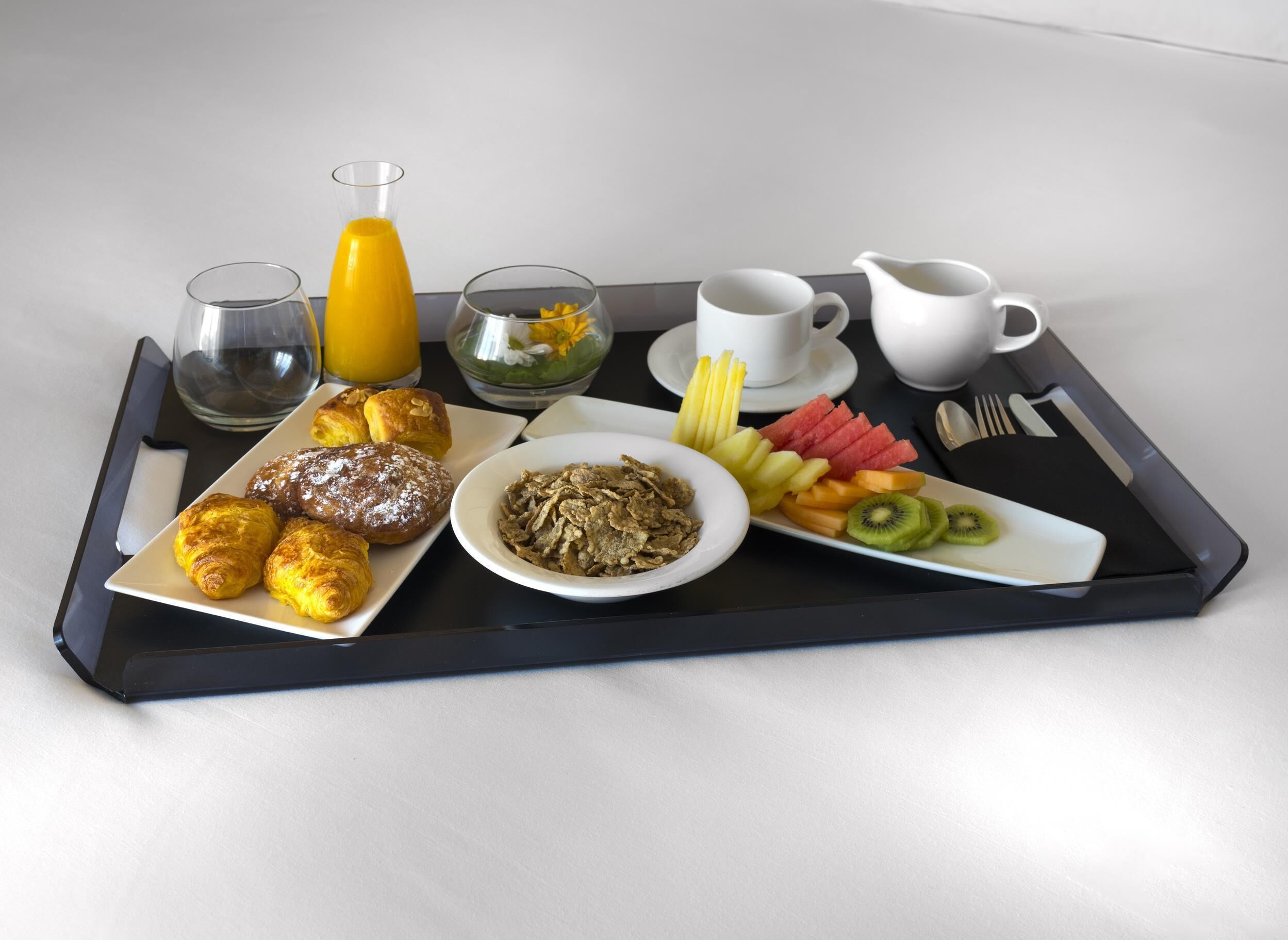 A tray with croissants, cereal, fruit, and a glass of orange juice.