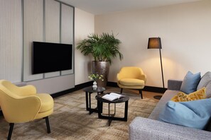 Un salon moderne avec un téléviseur à écran plat, deux fauteuils, un canapé, une table basse, un lampadaire et une plante en pot.