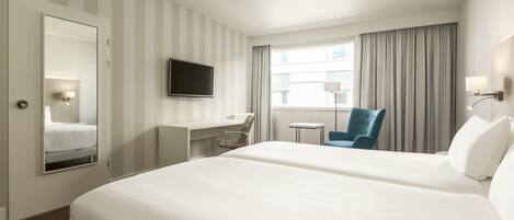 Habitación de hotel con una cama grande, un escritorio con silla, televisor montado en la pared y ventana con cortinas.