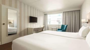 A hotel room with two beds, a desk, a chair, a TV, and a window with curtains.
