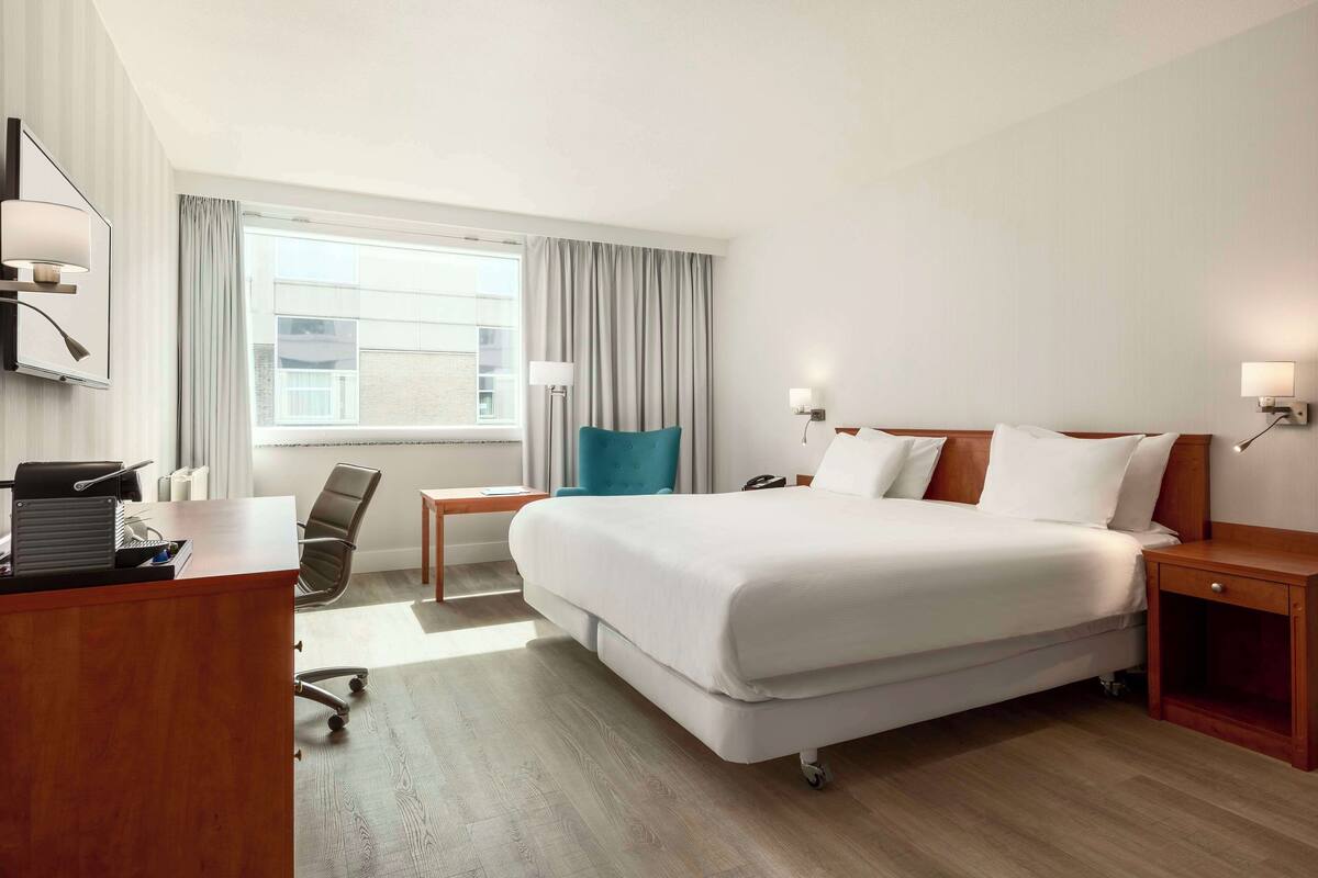 Habitación de hotel con una cama grande, un escritorio con computadora, una silla y una ventana con cortinas.