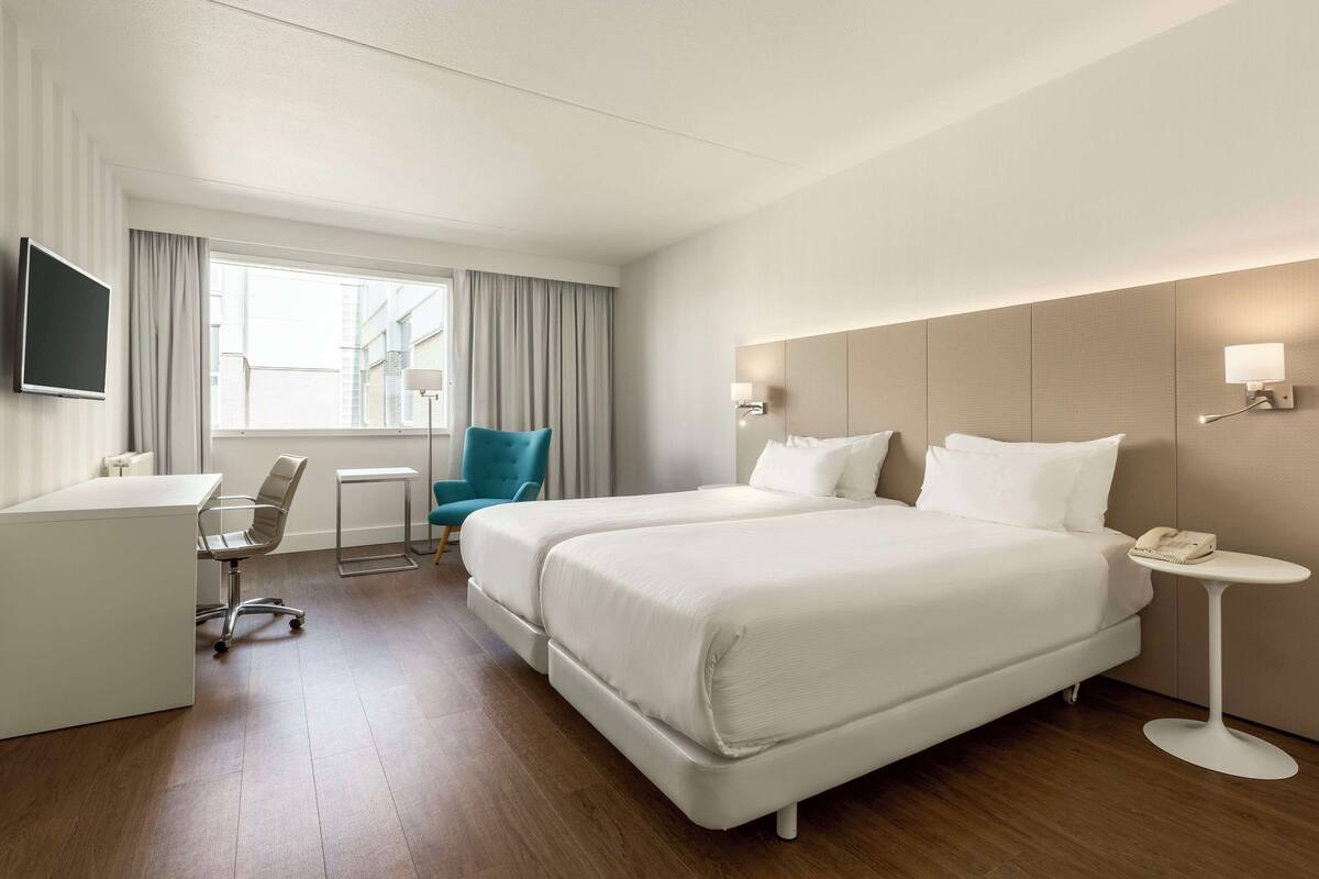 Una habitación de hotel con cama, escritorio, silla y una mesita.