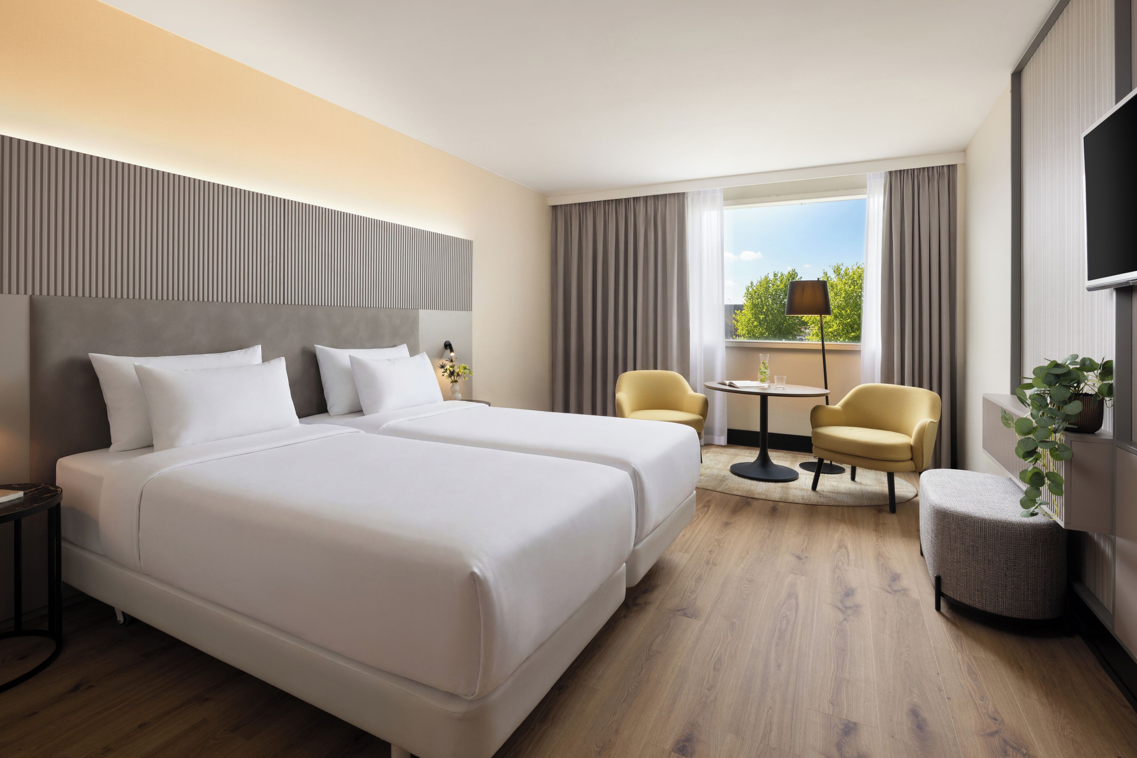 A hotel room with two beds, a small table, two chairs, a TV, and a window with curtains.