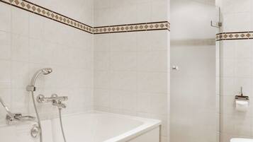 A bathroom with a white bathtub, a shower, and a toilet. The walls are tiled with a white and brown pattern.