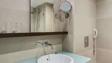 A bathroom with a glass sink, a mirror, a handheld showerhead, and a telephone.