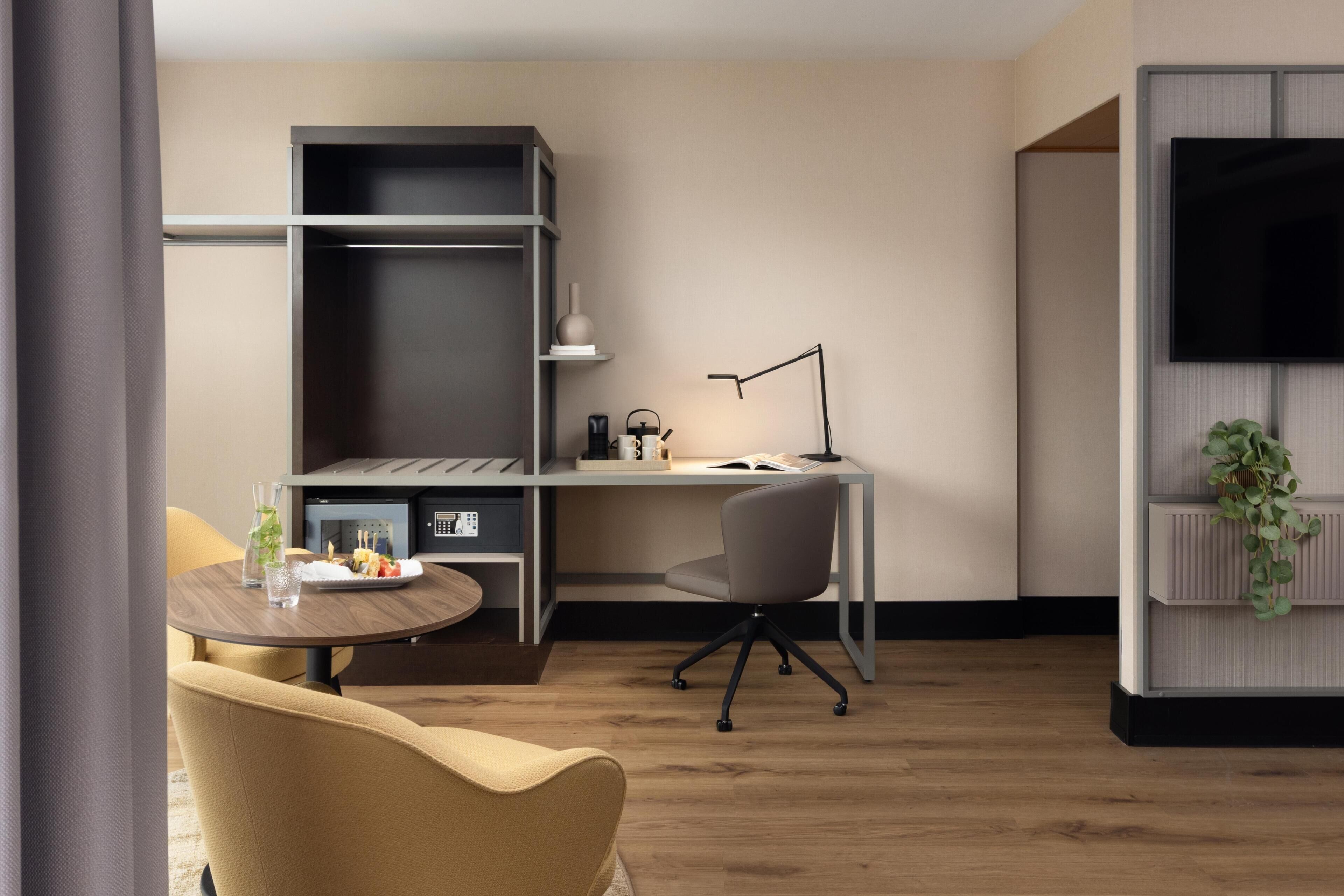 Une chambre d’hôtel moderne équipée d’un bureau, d’une chaise et d’un téléviseur fixé au mur.