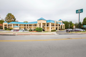 A multi-story motel with blue roofs and beige walls, featuring a central entrance and multiple parking spaces.