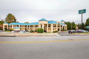 A multi-story motel with blue roofs and beige walls, featuring a central entrance and multiple parking spaces.