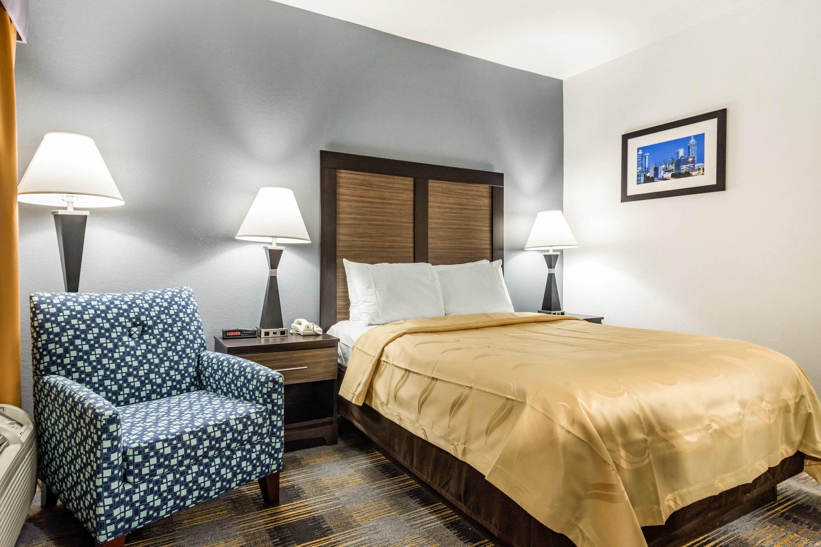 Ein Hotelzimmer mit einem Bett, einem Sessel, einem Nachttisch und einem an der Wand hängenden Bild.