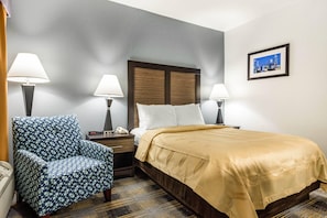 A hotel room with a bed, a chair, a nightstand, and a wall-mounted picture. - Quality Inn near Six Flags (Douglasville)