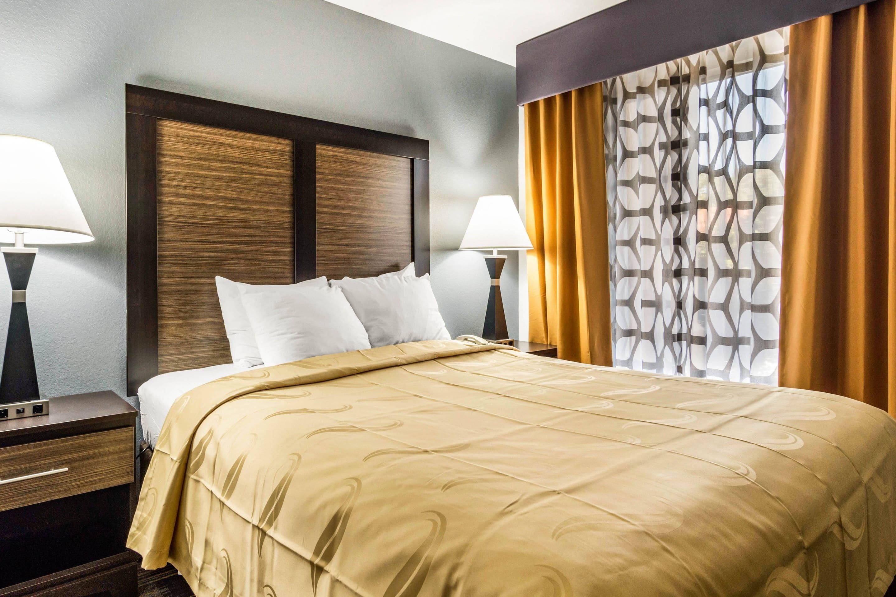 Een hotelkamer met een groot bed, twee nachtkastjes, een hoofdeinde en een raam met gordijnen.