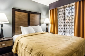 A hotel room with a large bed, two bedside tables with lamps, a headboard, and a window with patterned curtains. - Quality Inn near Six Flags (Douglasville)