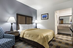 A hotel room with a bed, two bedside lamps, a chair, a nightstand, a mirror, and a picture on the wall.
