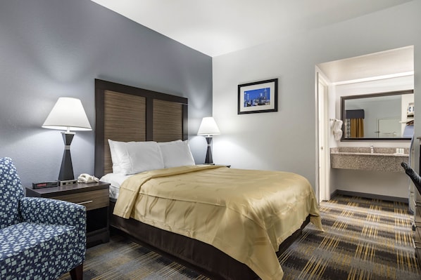 A hotel room with a bed, two bedside lamps, a chair, a nightstand, a mirror, and a picture on the wall.