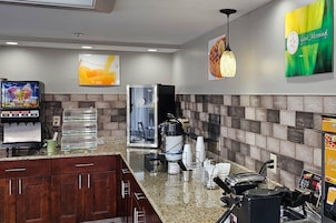 A hotel lobby with a coffee machine, a water dispenser, and a seating area with chairs and a table.