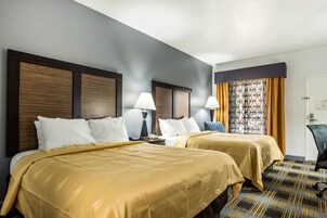 Habitación de hotel con dos camas, un escritorio, una silla y una ventana con cortinas.