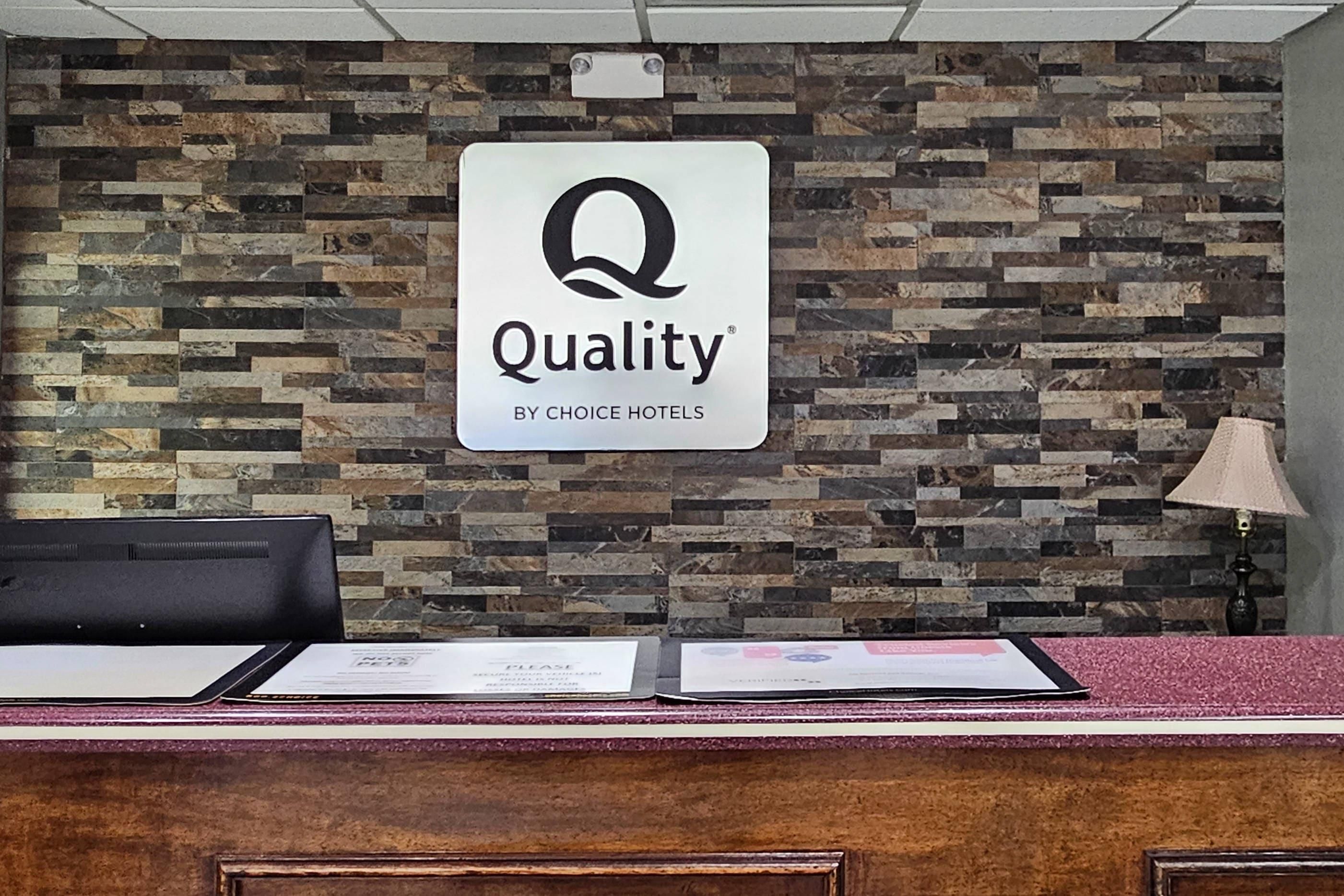 Ein Empfangstresen mit einem Schild, das 'Quality by Choice Hotels' an einer Wand mit Steinmuster zeigt.