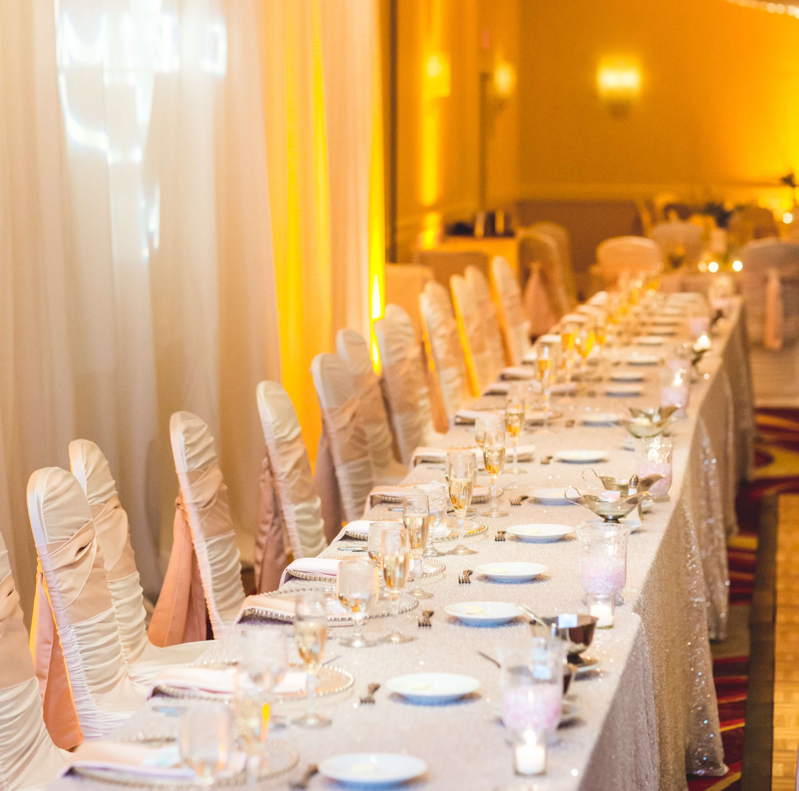 A banquet hall with long tables set for a formal event, featuring white tablecloths, glassware, and candles.