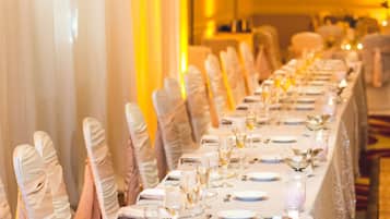 Une salle de banquet avec de longues tables dressées pour un événement formel, agrémentée de nappes blanches, de verres et de bougies.