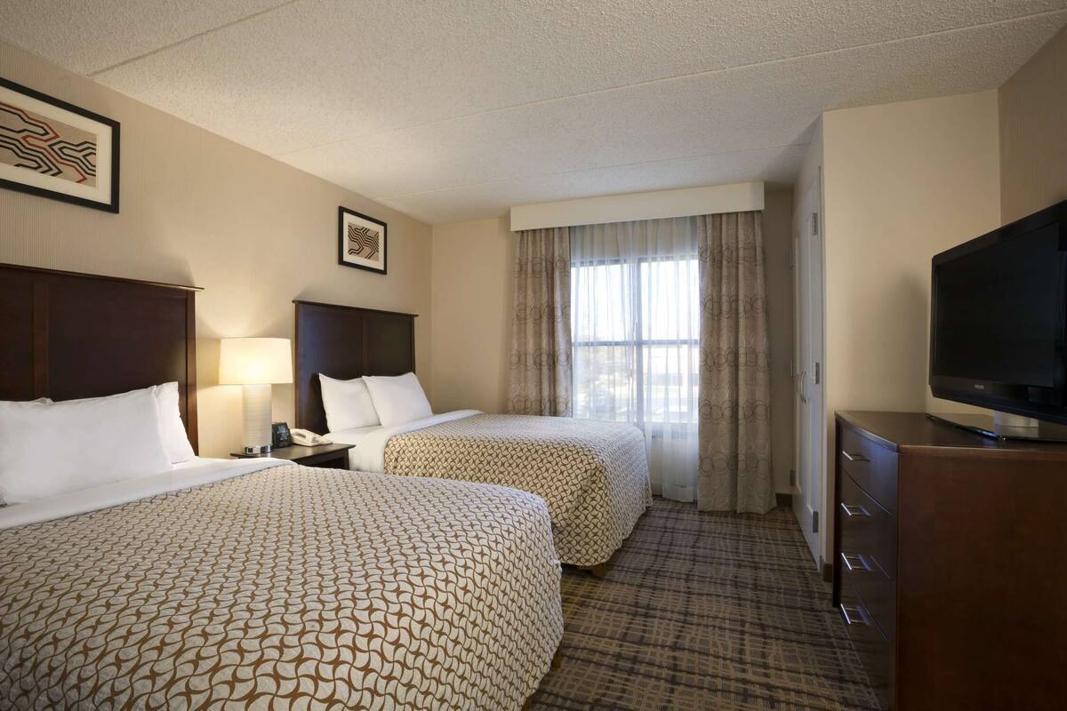 Habitación de hotel con dos camas, un televisor, un escritorio con lámpara y una ventana con cortinas.