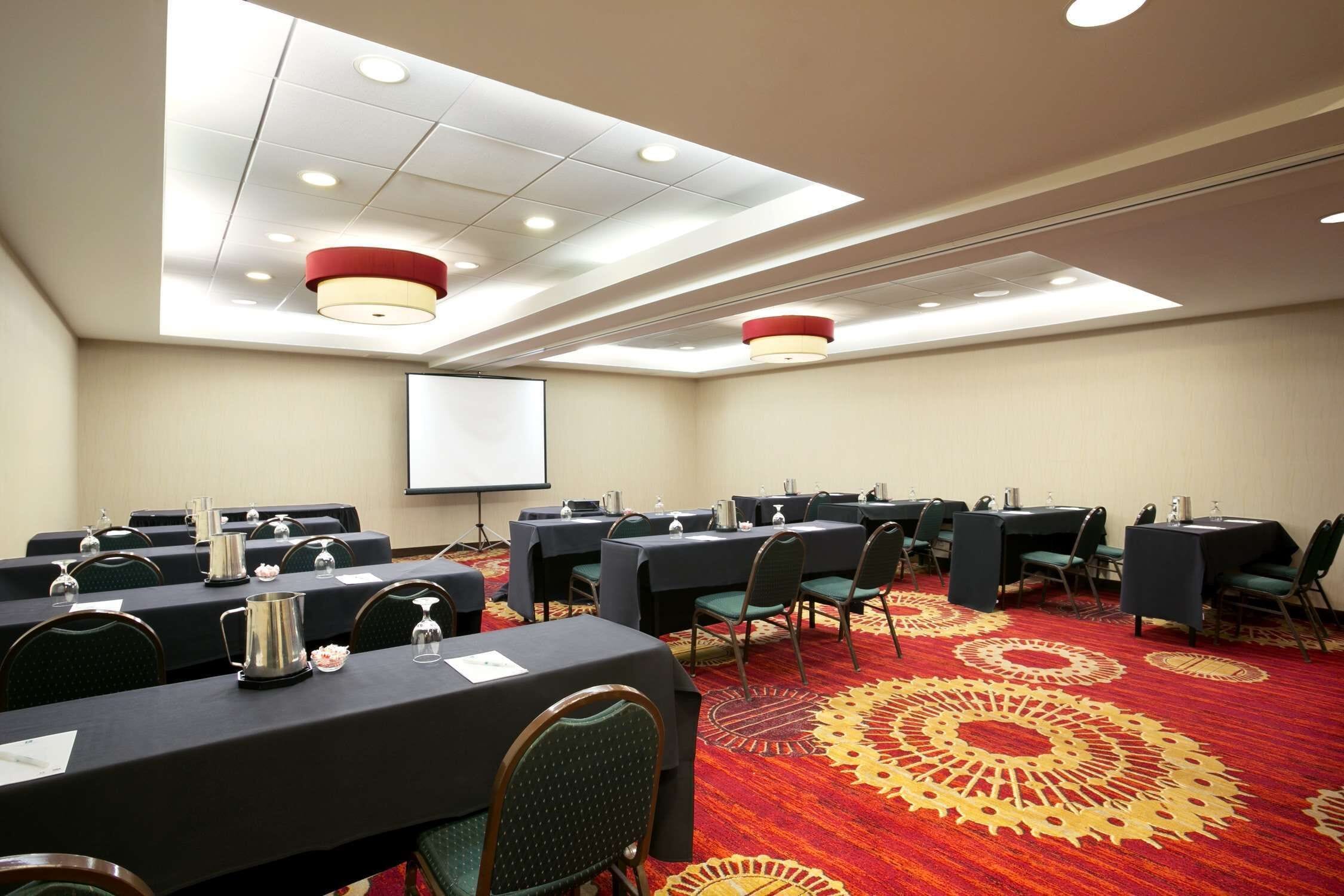 A conference room with tables, chairs, a projector screen, and a carpeted floor.